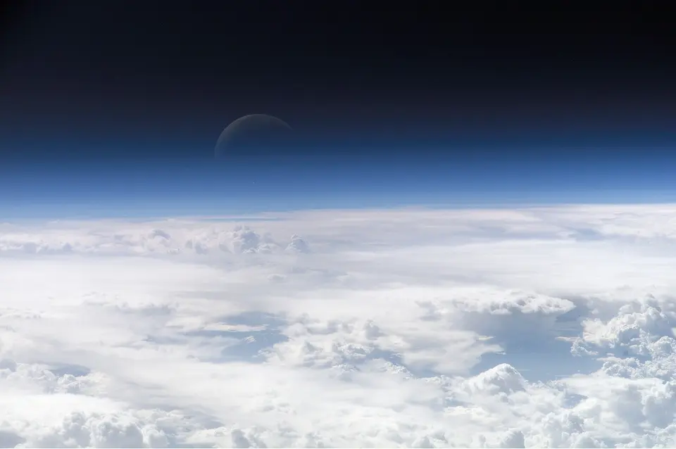 Modrý pás atmosféry nad zakřiveným zemským obzorem a Měsíc nad ním.