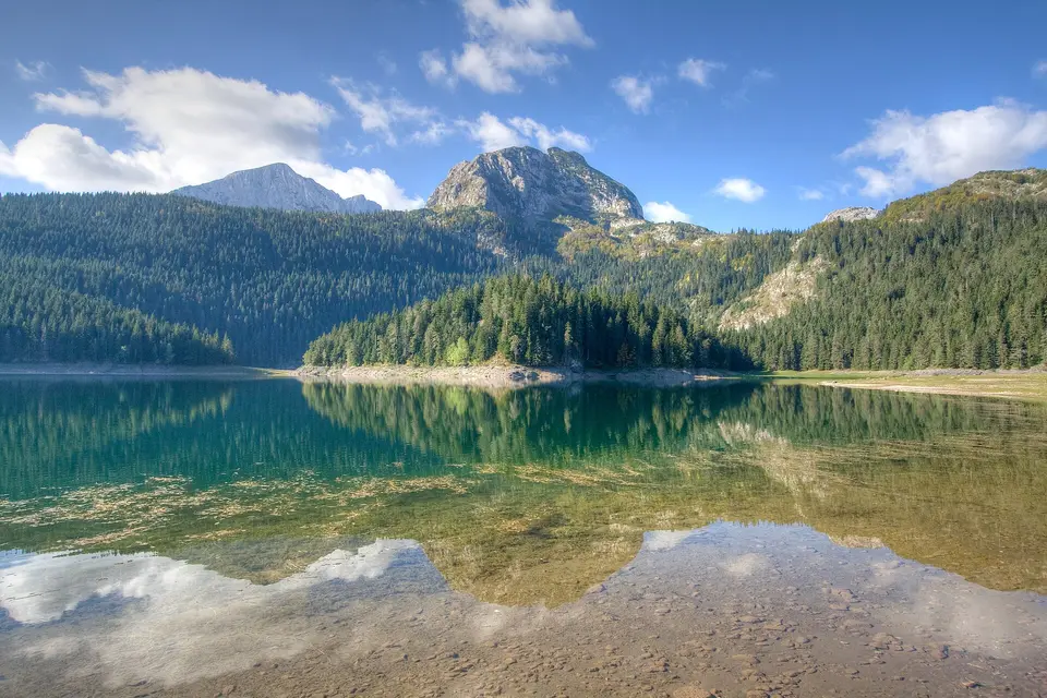 Horské jezero obklopené lesy a skalnatými vrcholy.