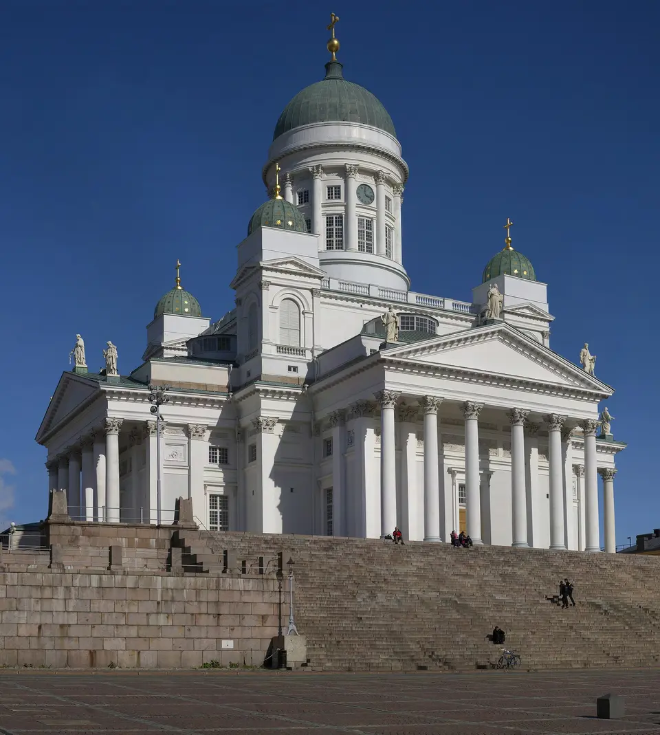 Bílá katedrála s zelenou kupolí nad helsinským náměstím.