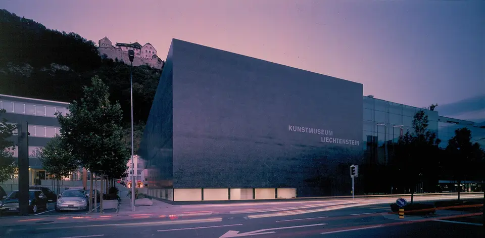 Tmavá kubická budova Kunstmusea Liechtenstein u ulice ve Vaduzu za soumraku.