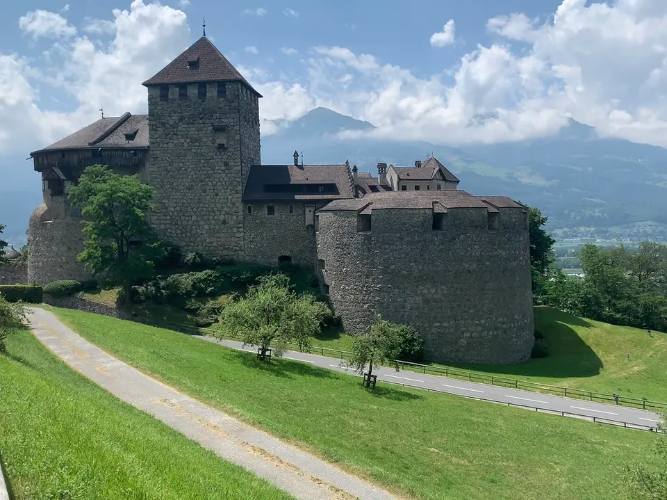Hrad Vaduz na svahu nad městem, v pozadí údolí Rýna a alpské vrcholy.