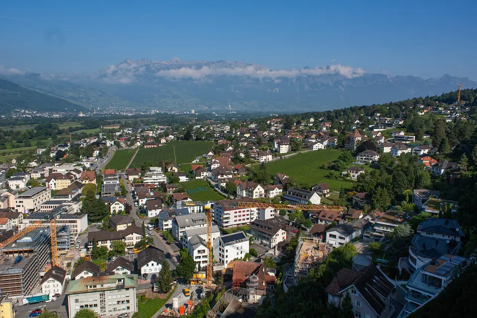 Panorama centra Vaduzu s hustou zástavbou v údolí a alpským svahem v pozadí.