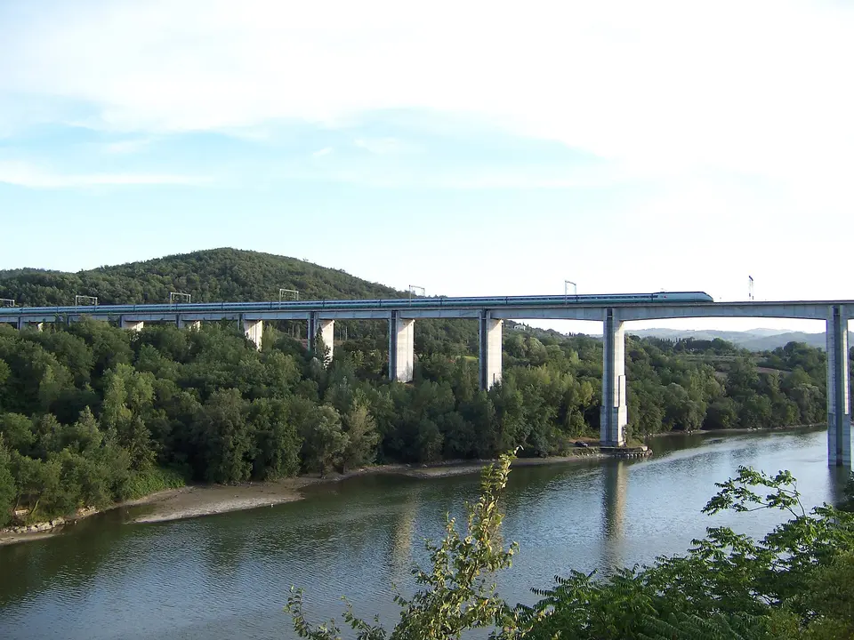 Vysoký železniční viadukt přes řeku v zeleném údolí.